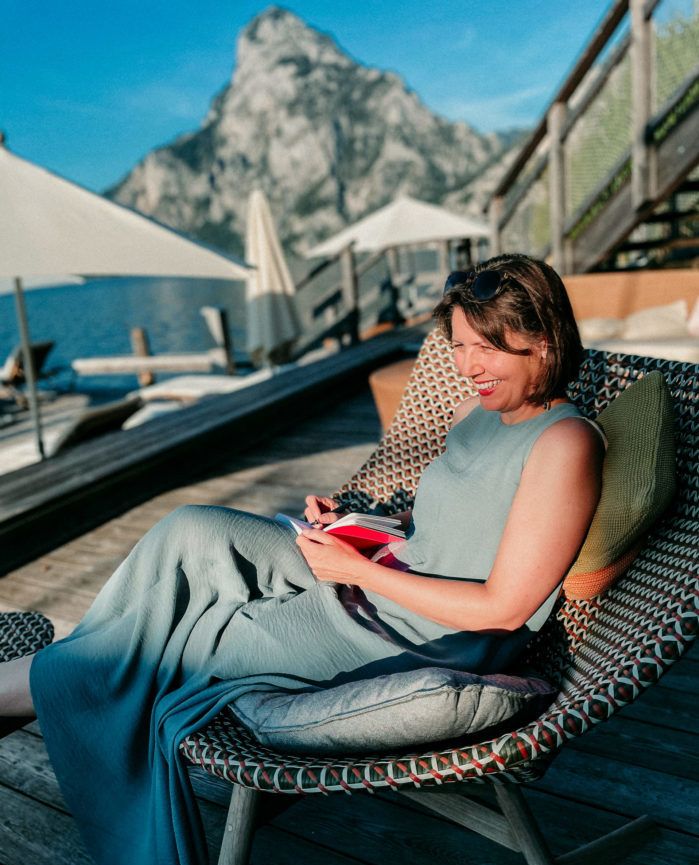 Woman sitting in a comfortable chair with a notebook in her hand, a lake and a mountain behind her