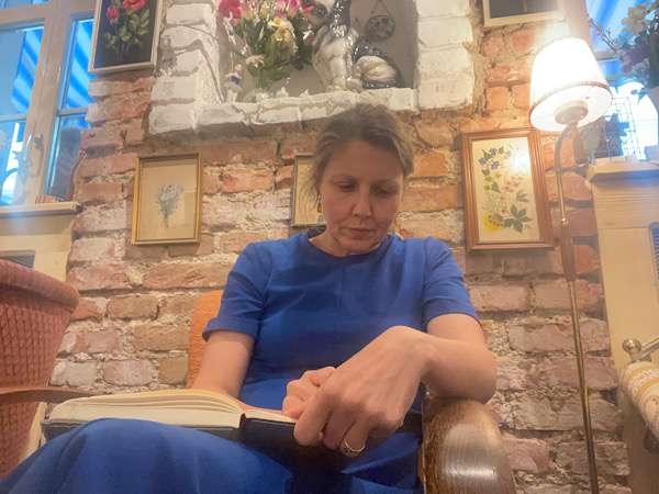 Woman in a blue dress sitting in a coffee shop and writing in her diary