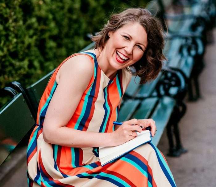 Woman in a colorful dress sitting on a bench, laughing, holding a notebook