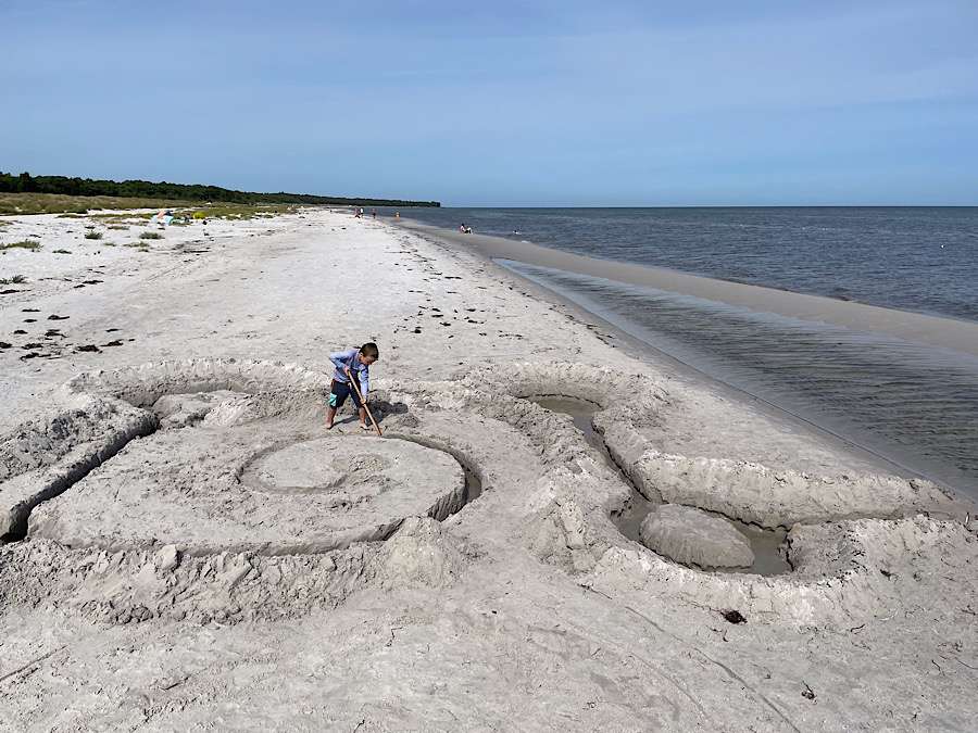 child digging in the sand on a long sandy beach