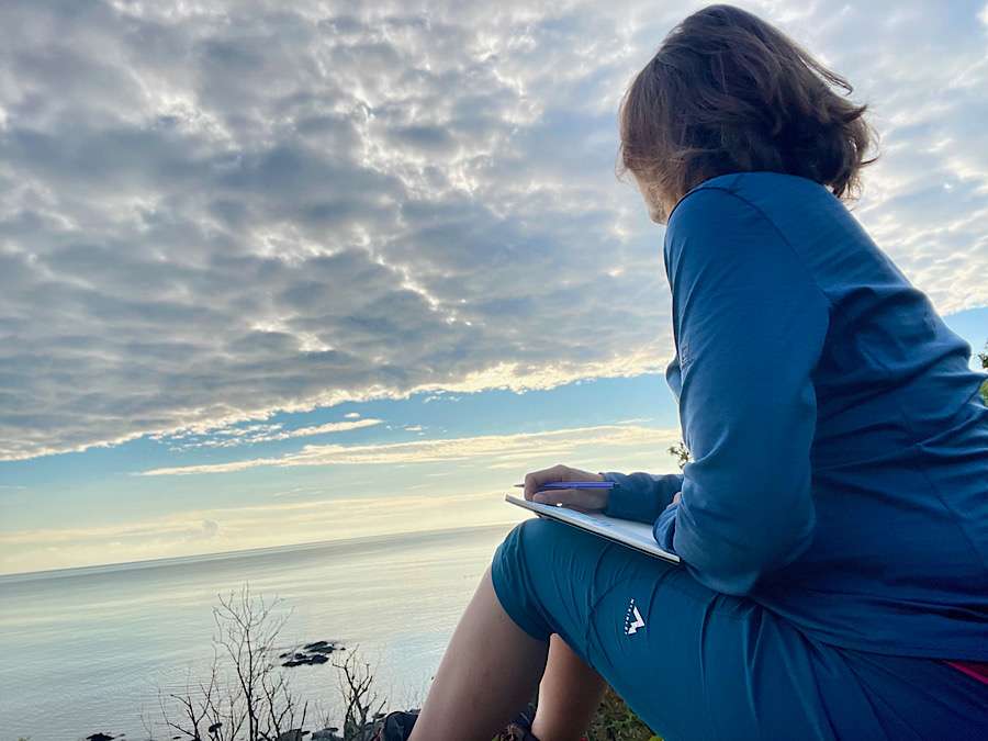 Woman sitting on a cliff overlooking the sea, a notebook for creative writing in her hand