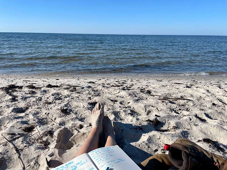 Bare feet and a notebook for creative writing on the sandy beach, sea in background