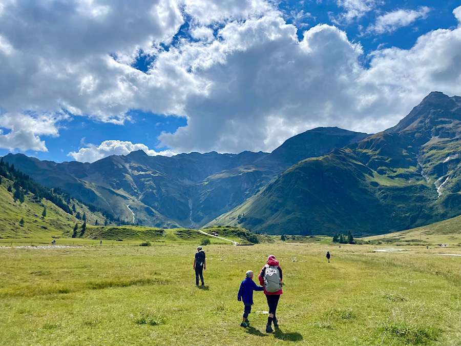Family walking on green grass, mountains and blue sky in background